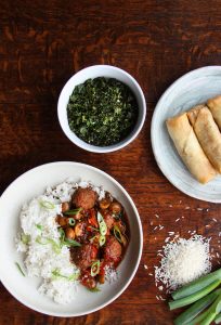 Table setting that includes black pepper vegan meatballs and rice, crispy kale and spring rolls